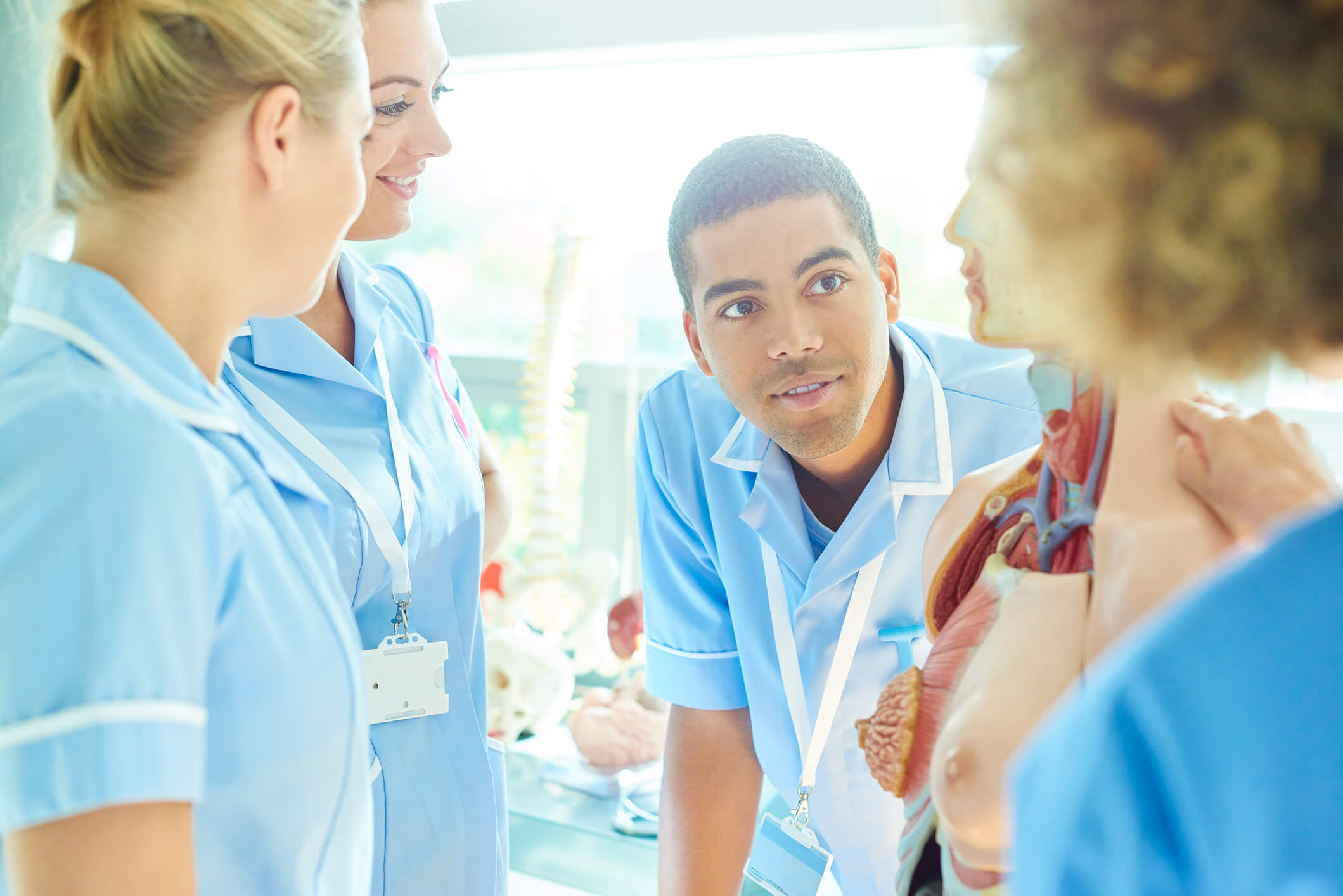 a group of male and female medical students listen to their tutor as she explains the various parts of an anatomical model