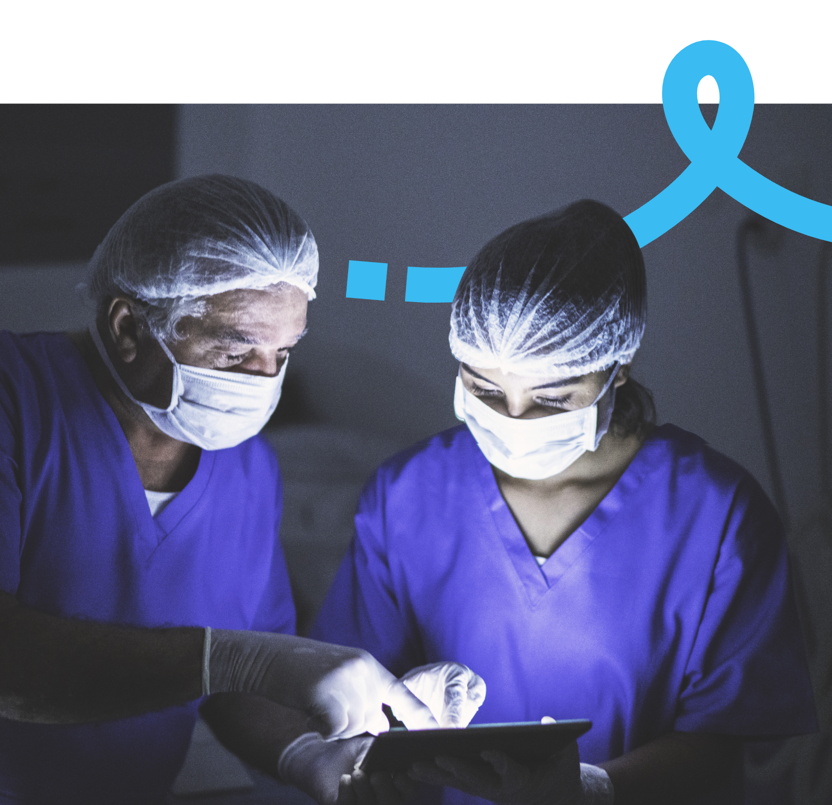 Two surgeons looking at a digital tablet in a low lit room, the focus is on the surgeons