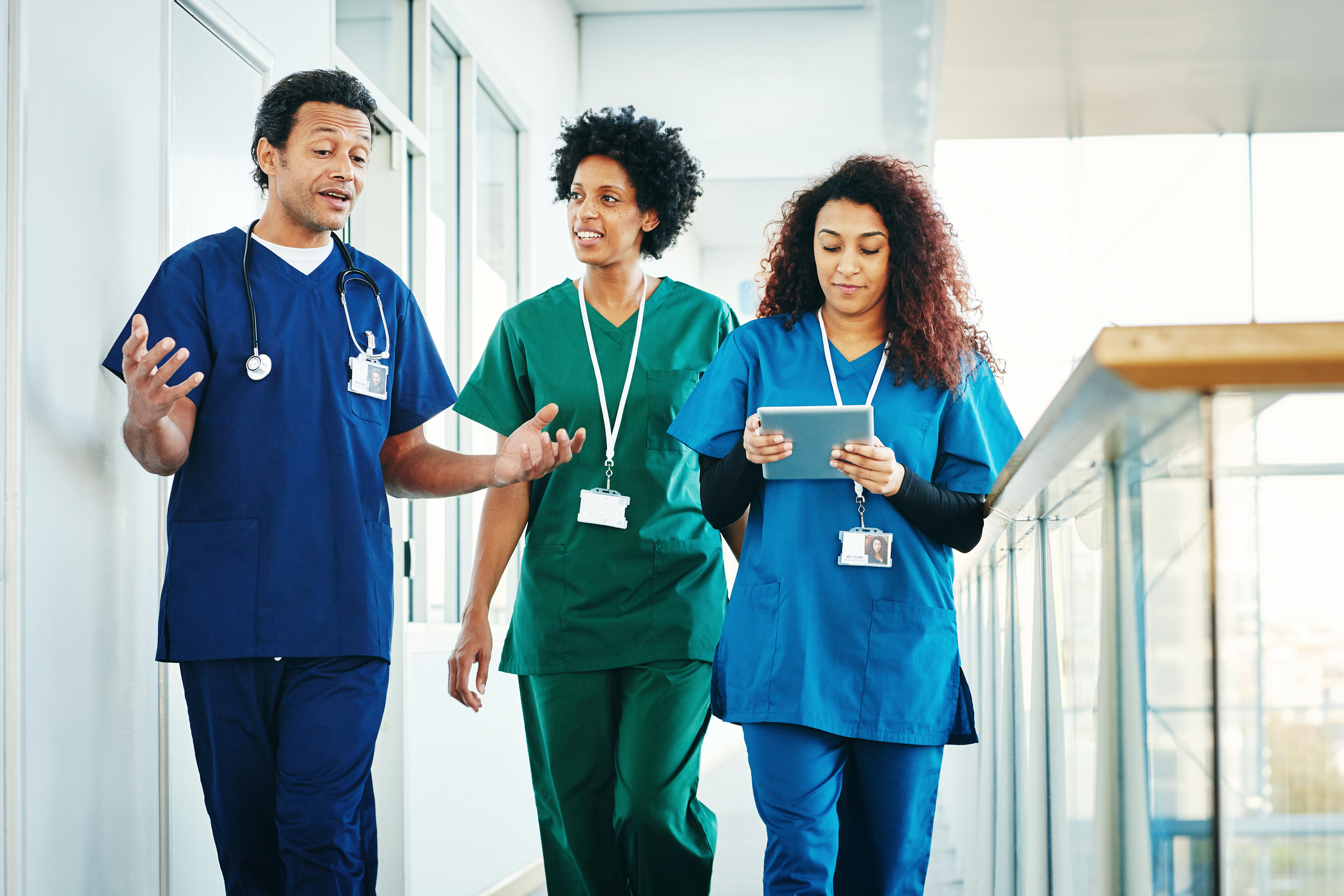 Group of medical professionals with digital tablet discussing along hospital corridor. Doctor and nurse walking together and talking.