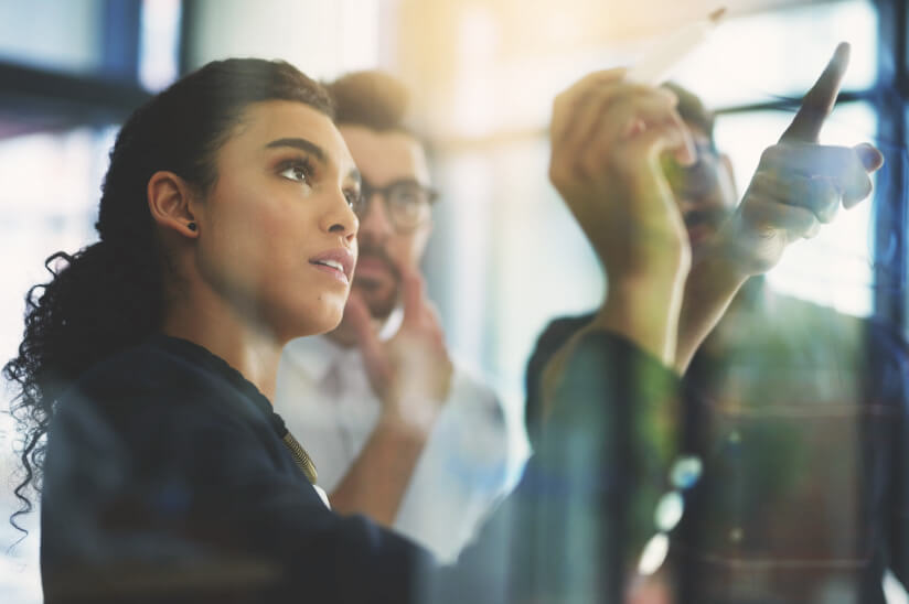 Shot of a group of colleagues brainstorming together on a glass wall in an office