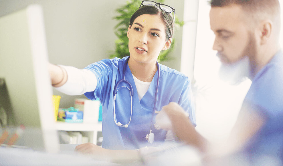 young medical professional discussing notes with her colleague at her desk