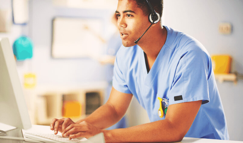 healthcare professional at computer wearing headset and typing on a computer in a hospital ward