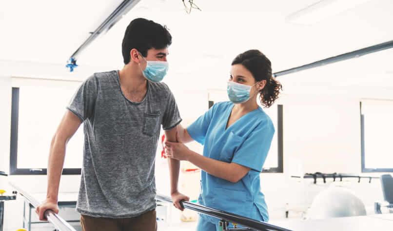 A HCP is helping a patient walk during a physio session