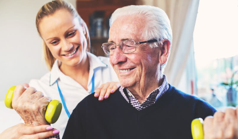 A professional is helping a patient lift weights during a physio therapy home visit session