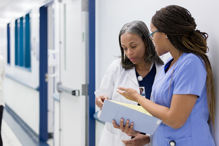 Female nurse and female doctor discuss patient care in a hospital corridor