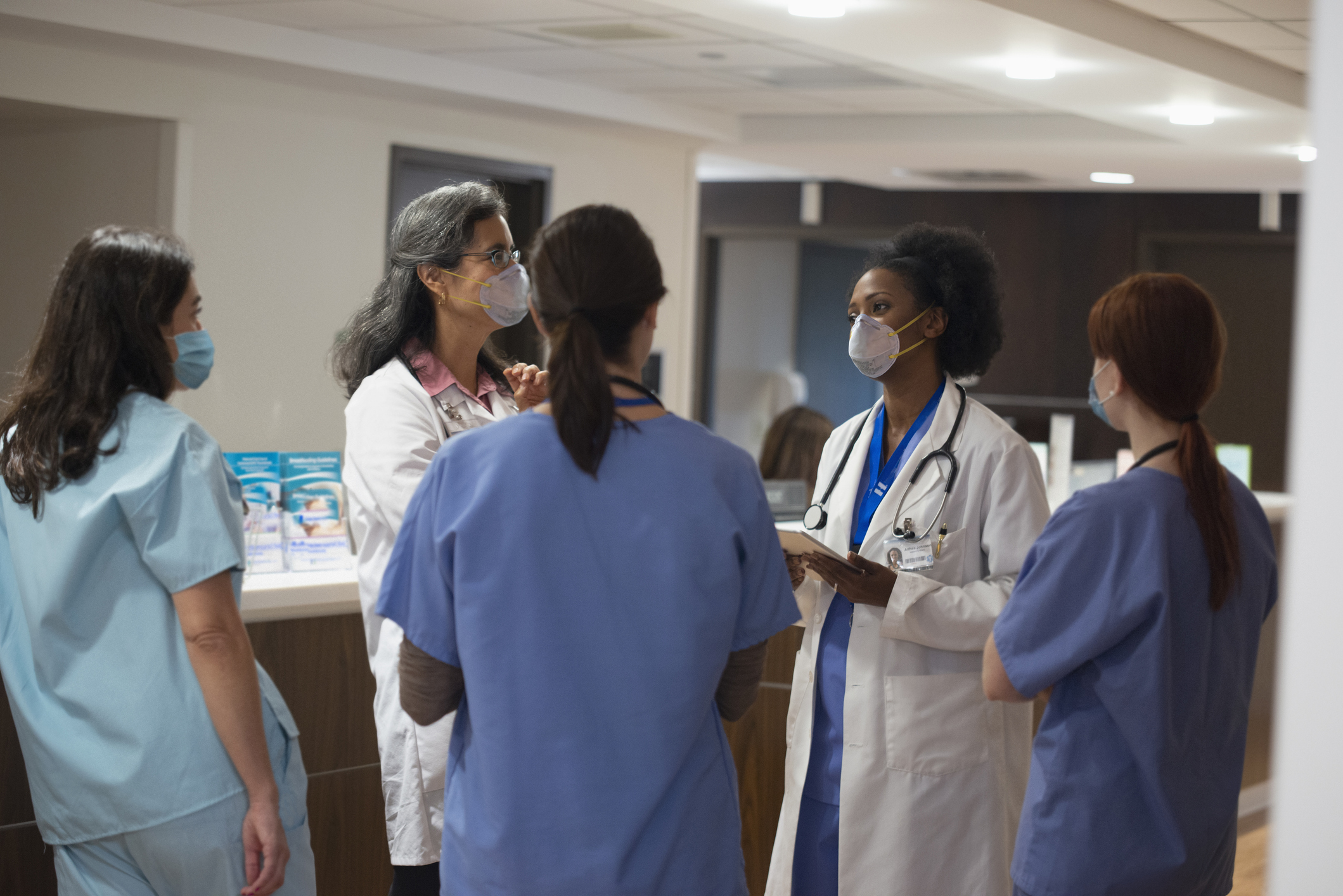 A group of five female doctors are talking in a hospital lobby near a desk