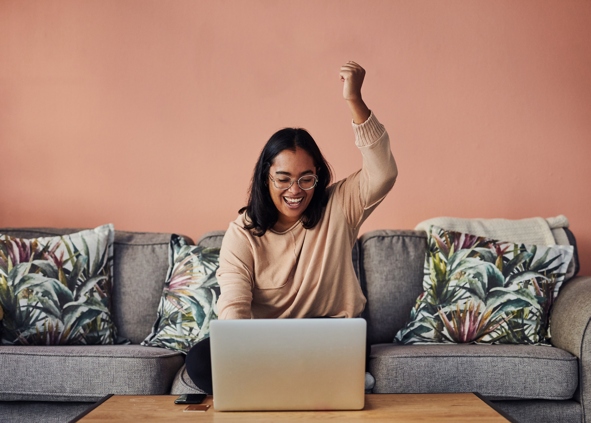 Shot of a young woman cheering while using a laptop on the sofa at home