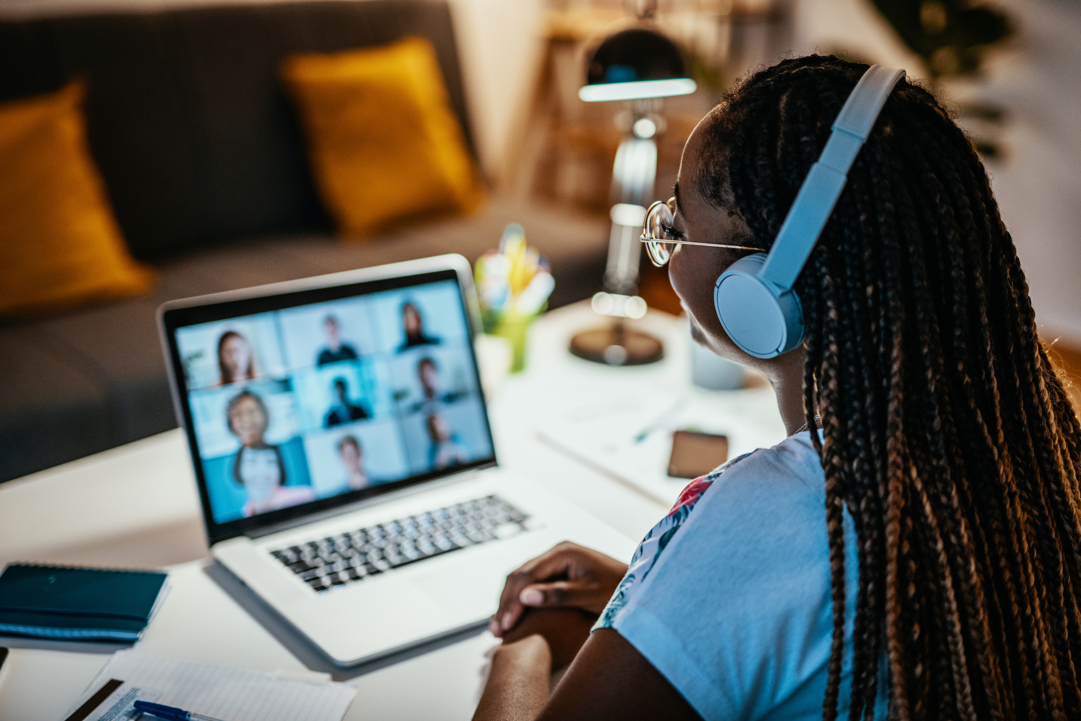 A woman is sitting at her desk wearing headphones while on a conference call on her laptop at a desk while working