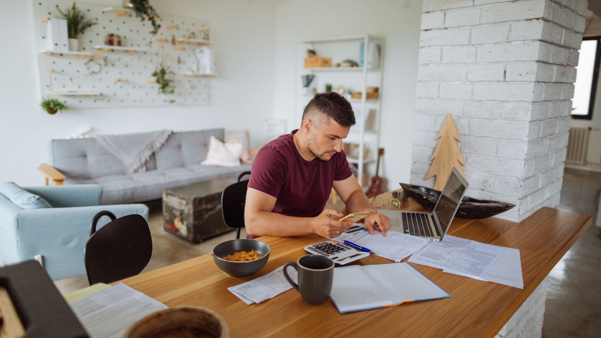 Young man at home, paying bills online using a laptop on a kitchen counter