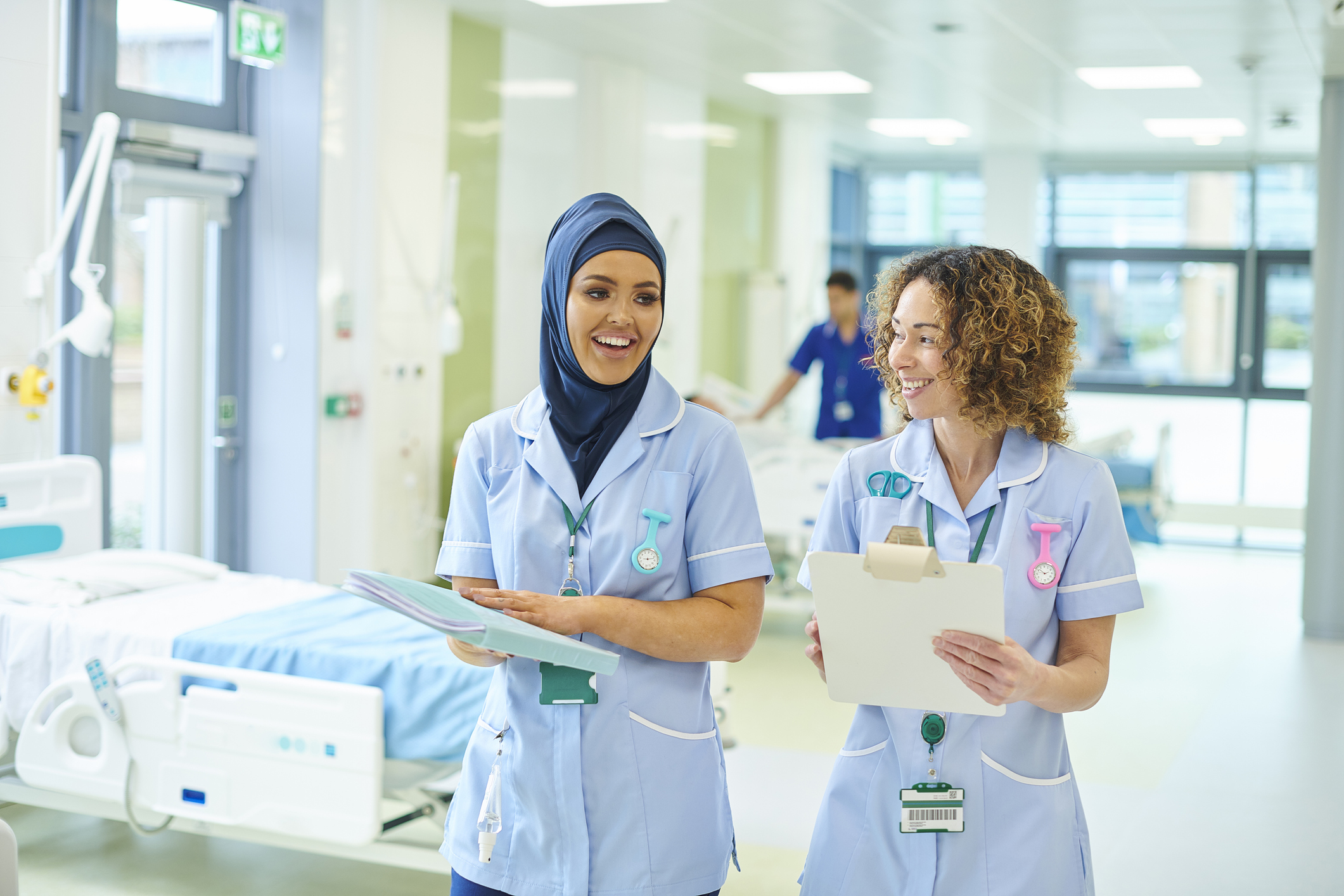 Two nurses in a happy discussion while conducting their rounds on a hospital ward holding clipboard and wearing nurse uniforms