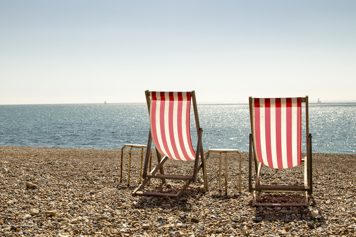 Landscape colour photo of a pair of red and white striped deckchairs on a stoney beach