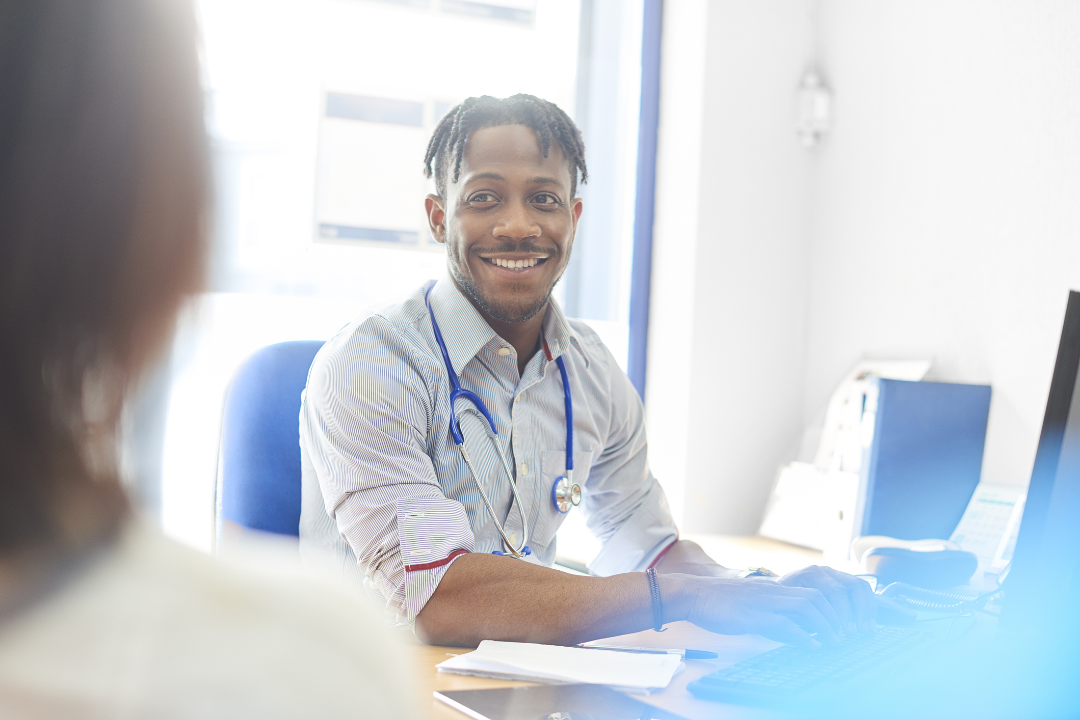 Junior doctor at his desk in his office in consultation with a patient