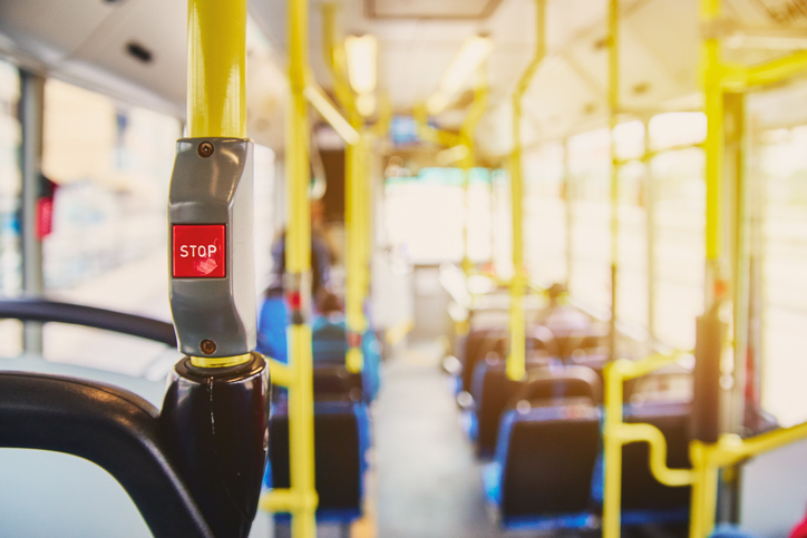 Red button STOP on the bus. Bus with yellow handrails and blue seats. Photo with the sun effect, glare on the lens from the light. Spacious interior of the bus, bright button with focus