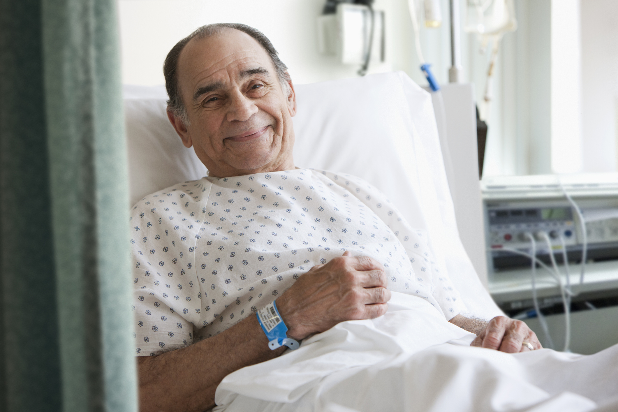 An elderly male patient is awake and sitting up in a hospital bed