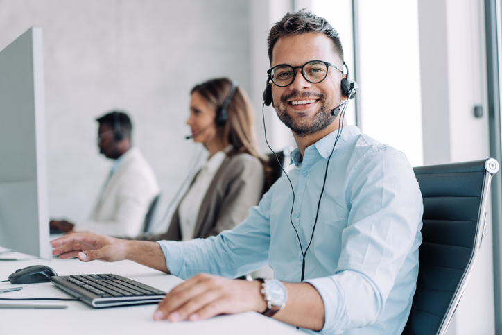 Shot of call center operators working in the office. Call center agent working with his colleagues in modern office. Smiling while working in call center.