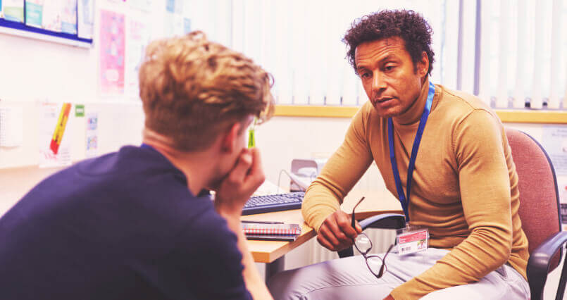 Male GP holding his glasses in deep conversation with male patient