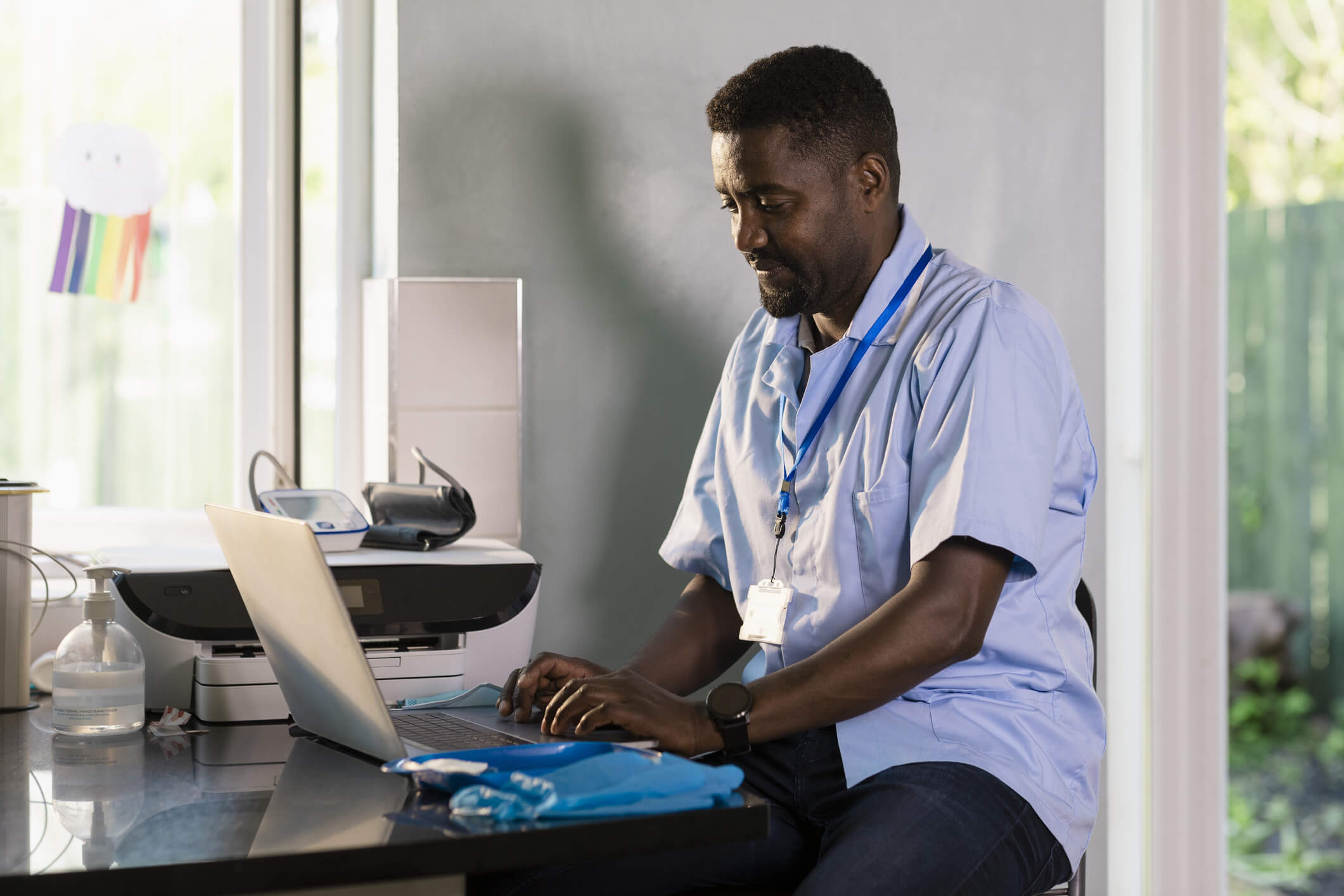 Side-view of a male doctor wearing his uniform. He is working hard at a desk in his office, using his laptop.