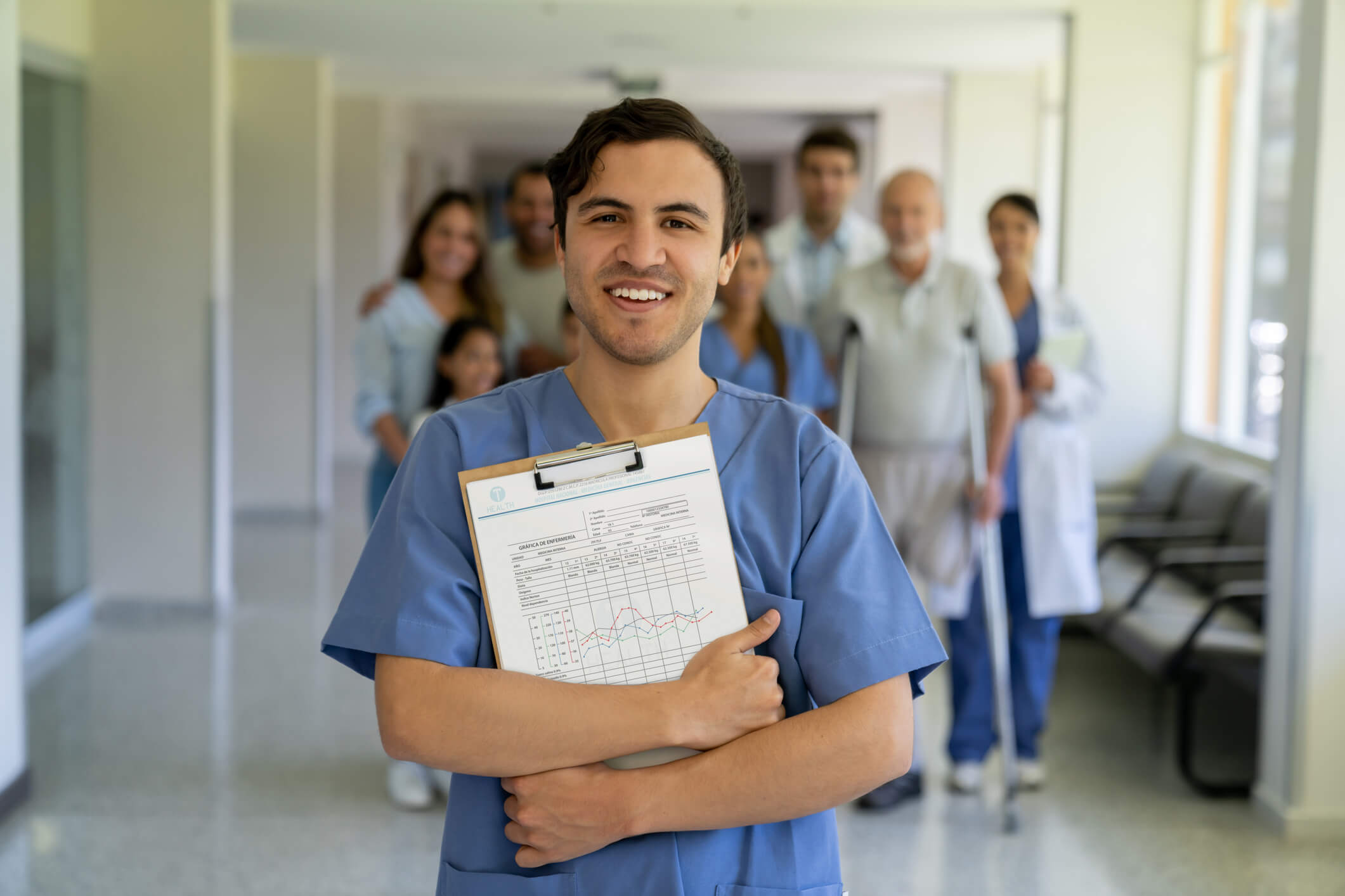 Portrait of a happy male doctor smiling at the hospital with patients and healthcare workers at the background