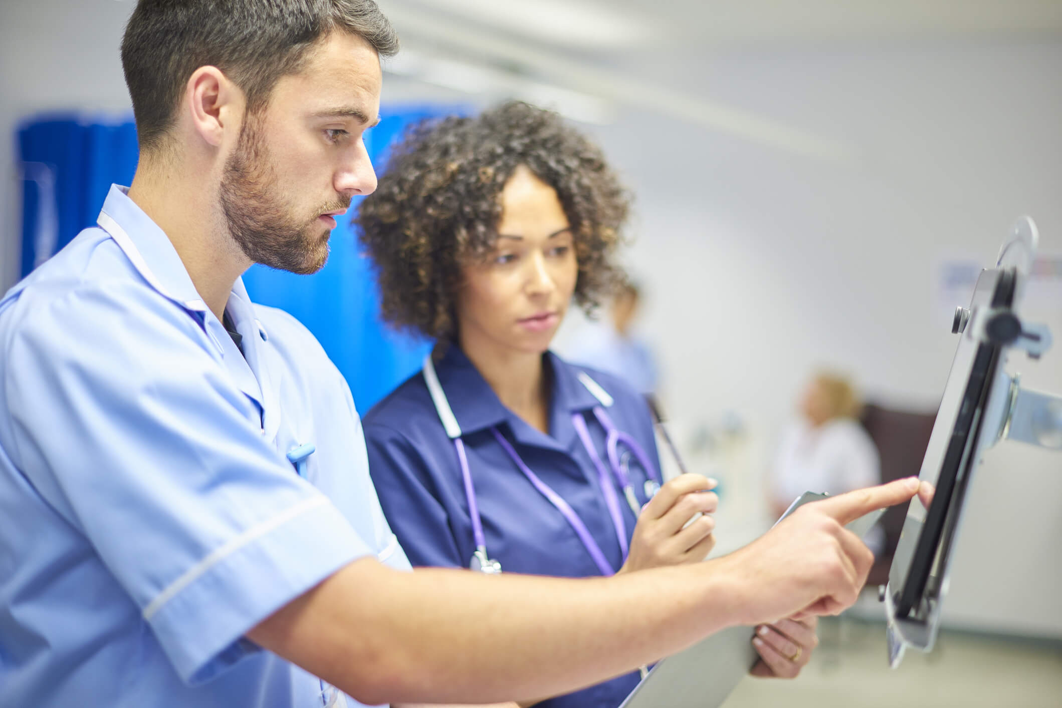 A male nurse checks the dosage on his digital tablet supervised by his staff nurse