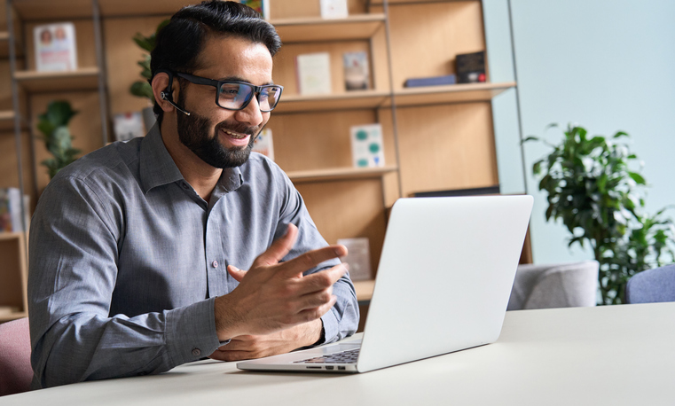 Happy indian business man remote teacher, customer support manager wearing headset talking at virtual meeting consulting client on video call giving distance learning class at home office call center.