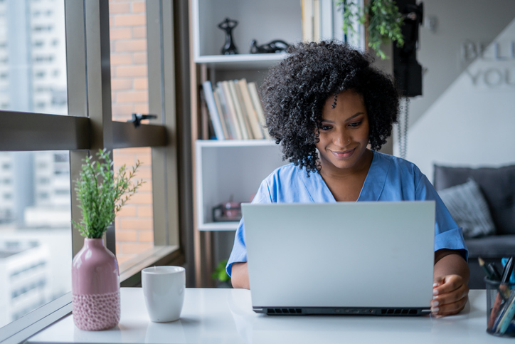 Nurse having a video consultation with a patient via a laptop in an office near a window