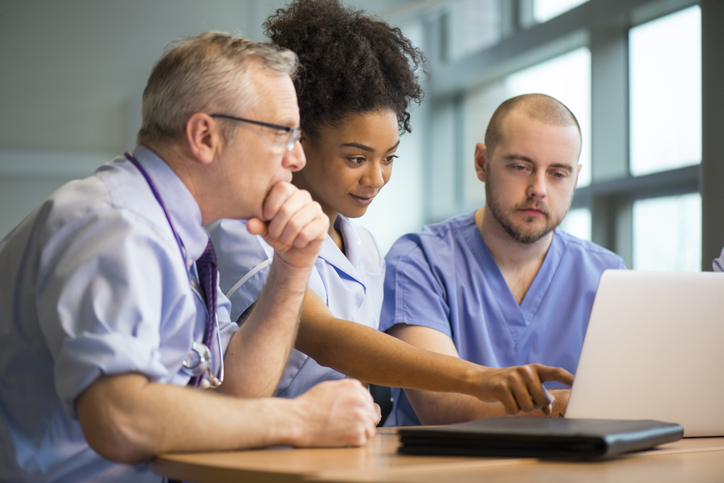 Medical staff meeting around a table in a hospital office using a laptop