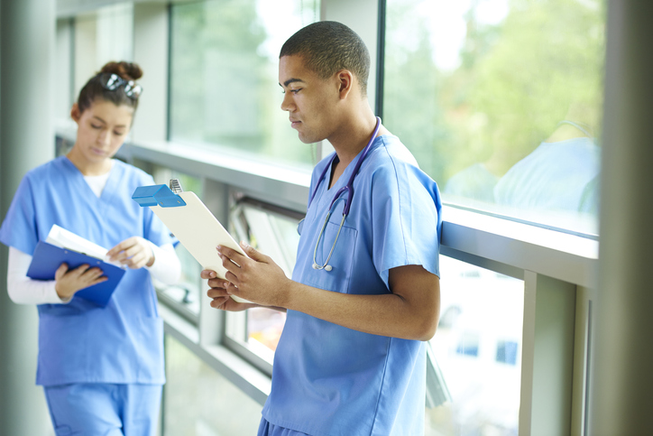 A young male and female nurse stand in the corridor of the hospital checking their medical notes.