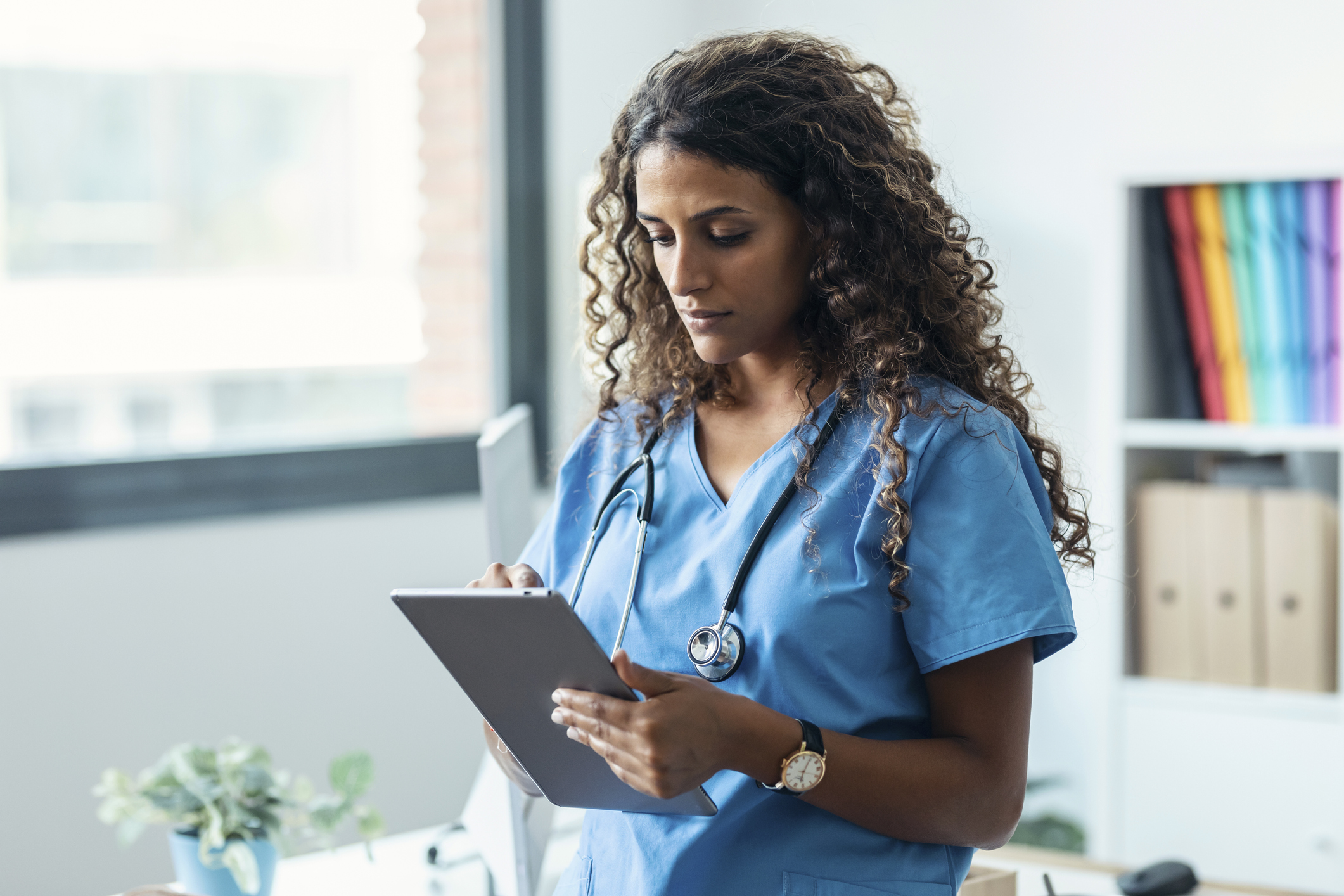 Female nurse using her digital tablet while standing in the consultation