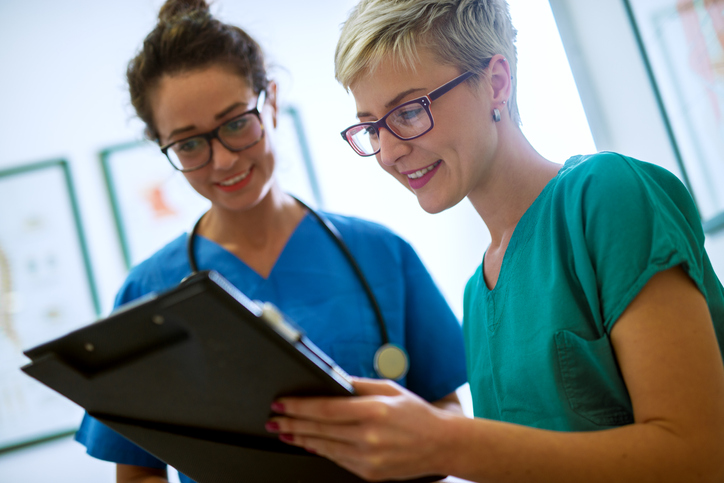 Close up view of two professional Nurses consulting data on a clipboard