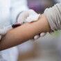 Woman donating blood and doctor holding the needle while it fills