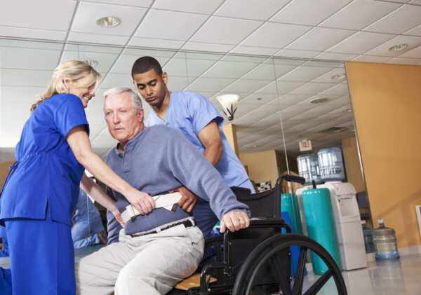 Physical therapists helping patient (60s) from treatment table into wheelchair.