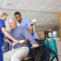 Physical therapists helping patient (60s) from treatment table into wheelchair.